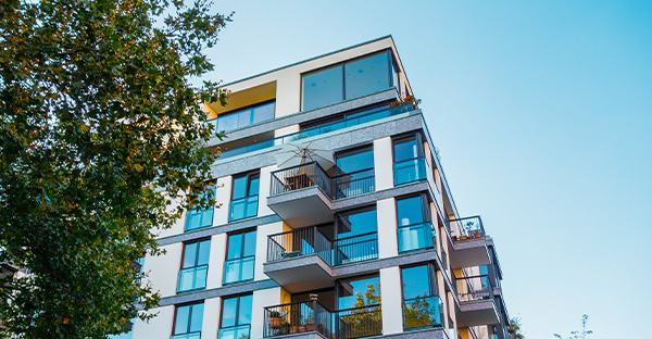 modern apartment building with balconies and large windows under clear blue sky featuring greenery in foreground and seventh floor design elements